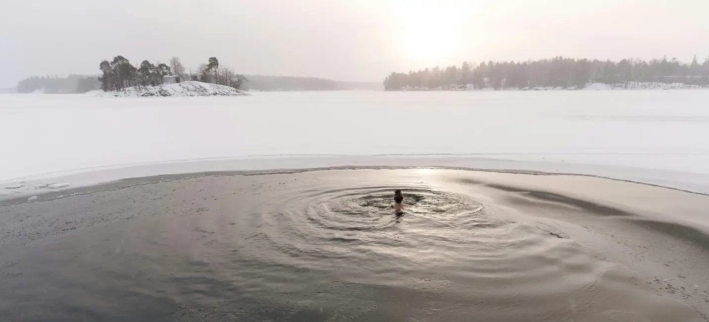 سبّاح وحيد يغطس في بحيرة متجمدة عند شروق الشمس – لحظة هادئة من القوة والتجدد وسط صمت الشتاء.