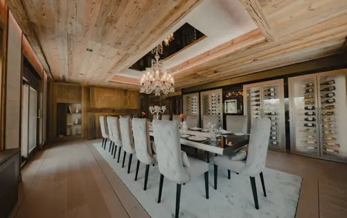 Salle à manger privée élégante dans un chalet alpin de luxe, ornée d’un lustre en cristal, de chaises en velours, d’une table raffinée et de caves à vin climatisées, pour des dîners intimes et des événements exclusifs.