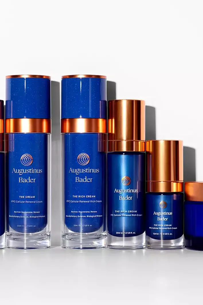 Collection of Augustinus Bader skincare products including The Cream, The Rich Cream, and The Body Cream in blue and copper packaging.