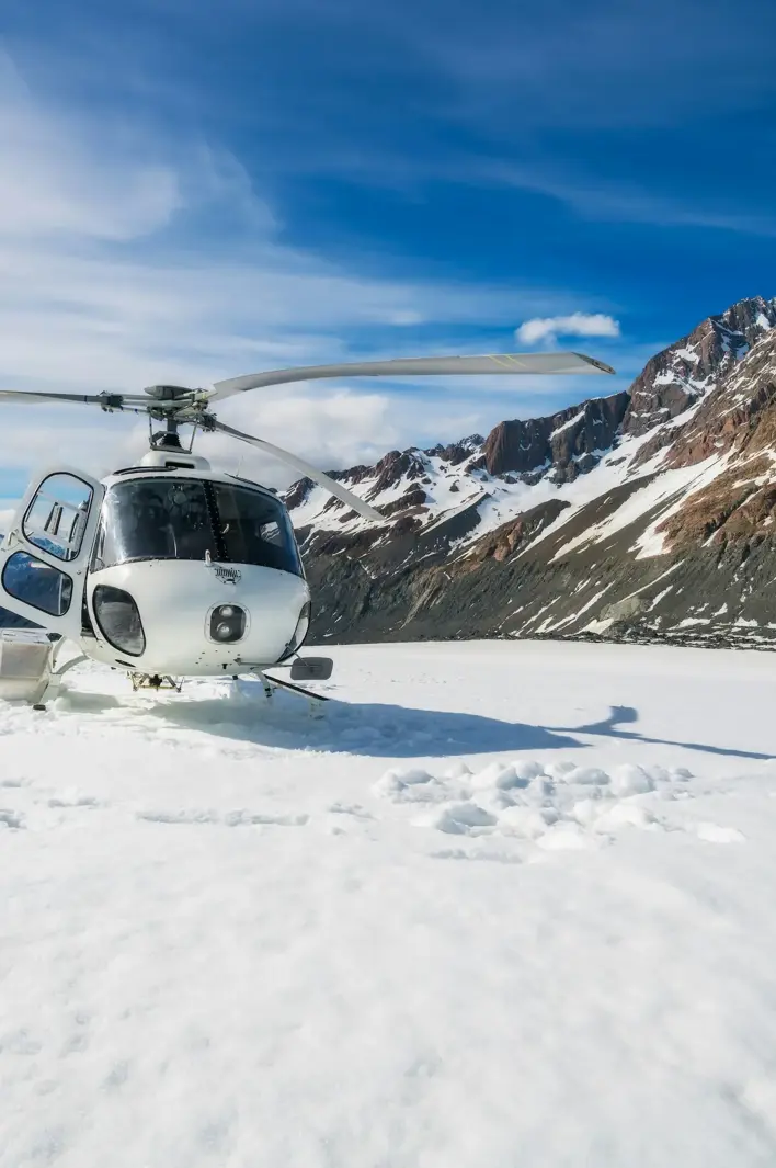 A helicopter rests on a pristine snowfield surrounded by rugged peaks and clear blue skies — the essence of alpine exploration.