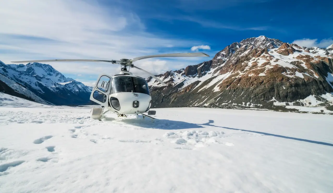 Un hélicoptère posé sur un champ de neige immaculé, entouré de sommets escarpés et d’un ciel bleu éclatant – l’essence même de l’aventure alpine.