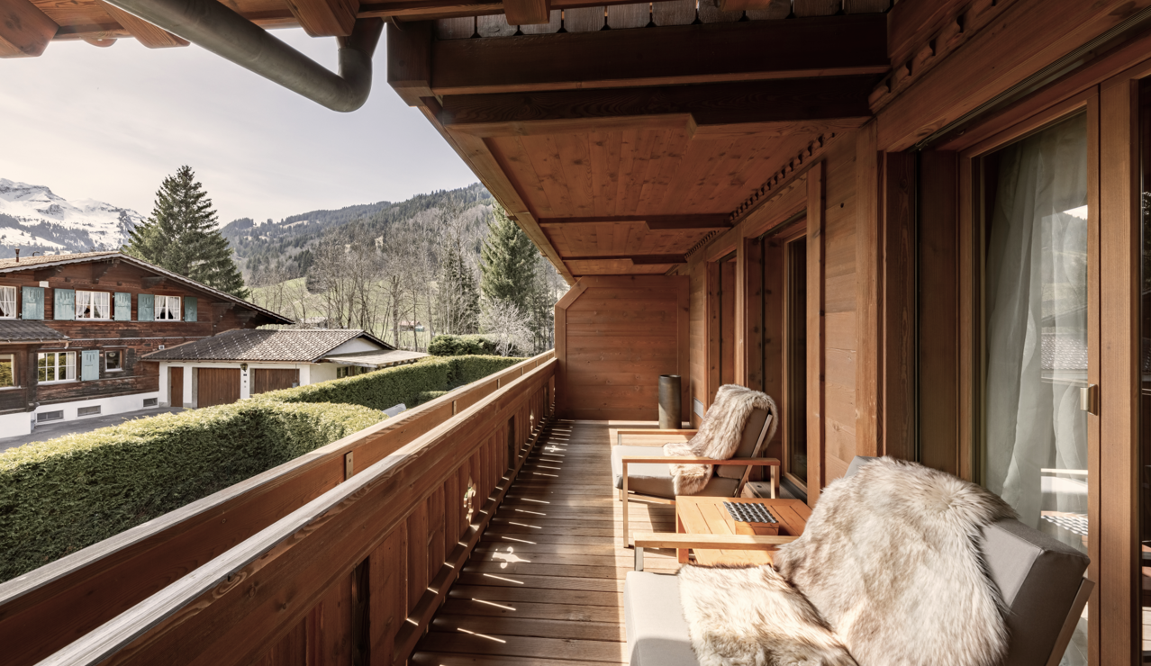 Wooden balcony with cozy fur-covered chairs overlooking alpine chalets and snow-capped mountains at Ultima Gstaad.