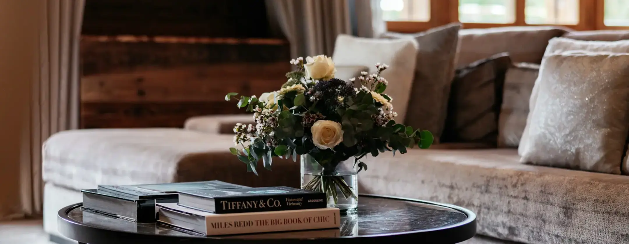 Elegant living room with wooden walls, soft neutral sofa, and a coffee table with flowers and design books.
