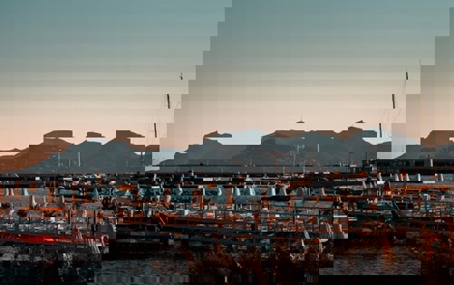 Scenic marina at sunset with calm water, docked boats, and mountains in the background.