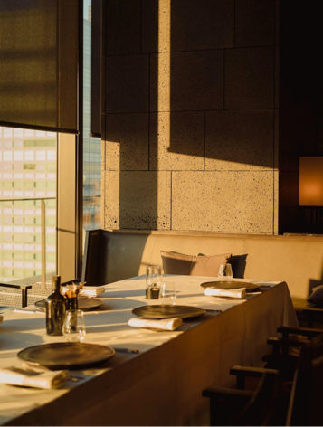 Elegant restaurant table set for dinner in warm evening light by a large window.