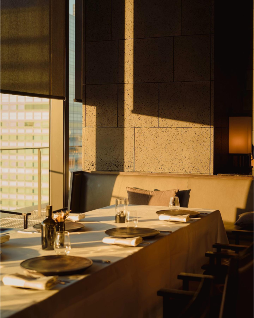 Elegant restaurant table set for dinner in warm evening light by a large window.