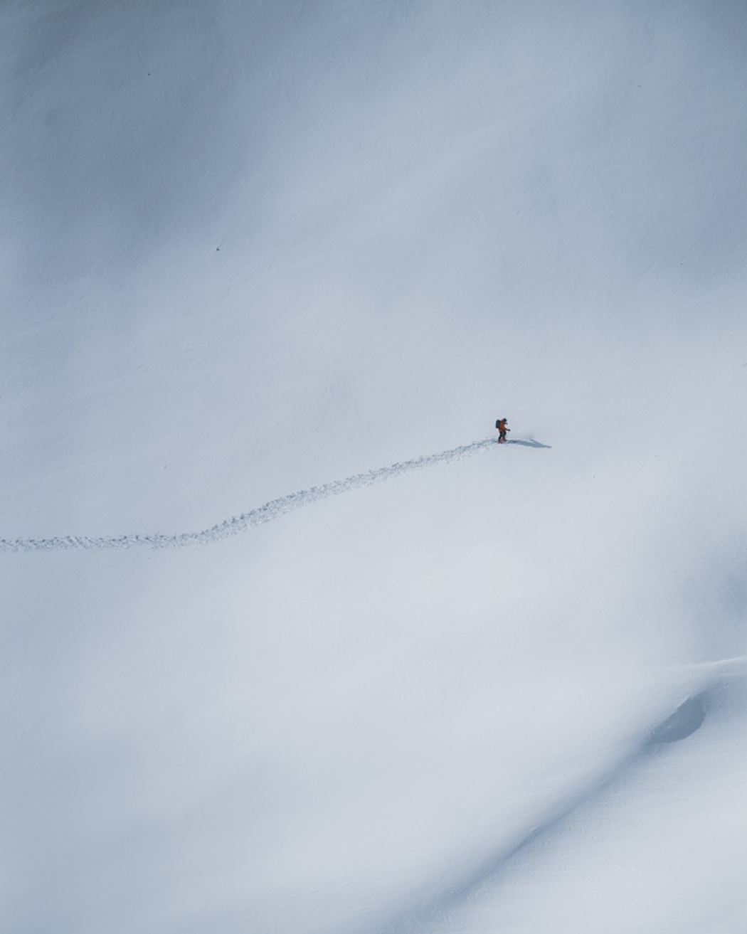 Solo skier making fresh tracks across untouched snow on a mountain slope.
