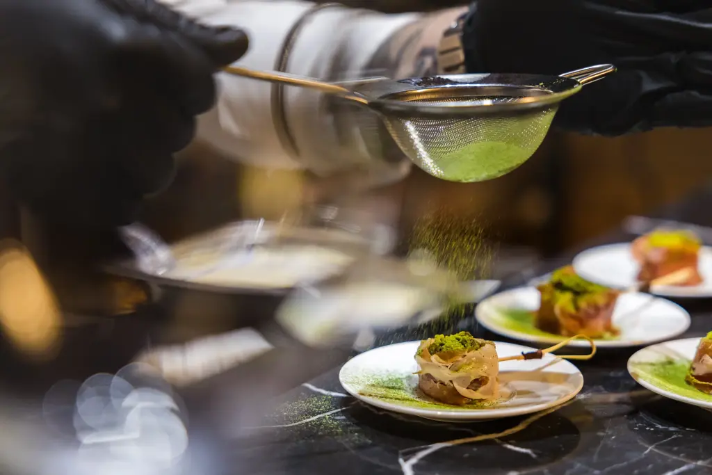 طاهٍ يرتدي قفازات سوداء يضيف اللمسة النهائية على طبق فاخر، في مشهد يجسد الإتقان والدقة وفن الطهو الراقي.