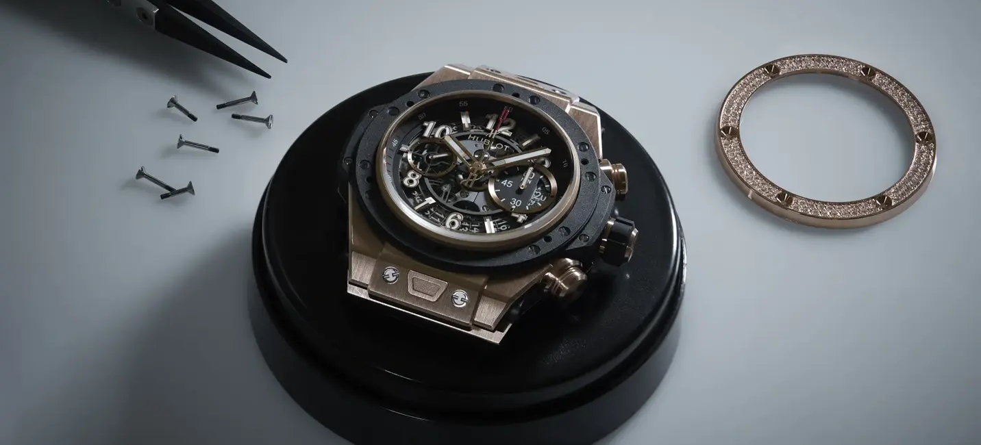 A luxury skeleton watch rests on a craftsman’s stand, surrounded by precision tools, screws, and a diamond-set bezel ready for assembly.