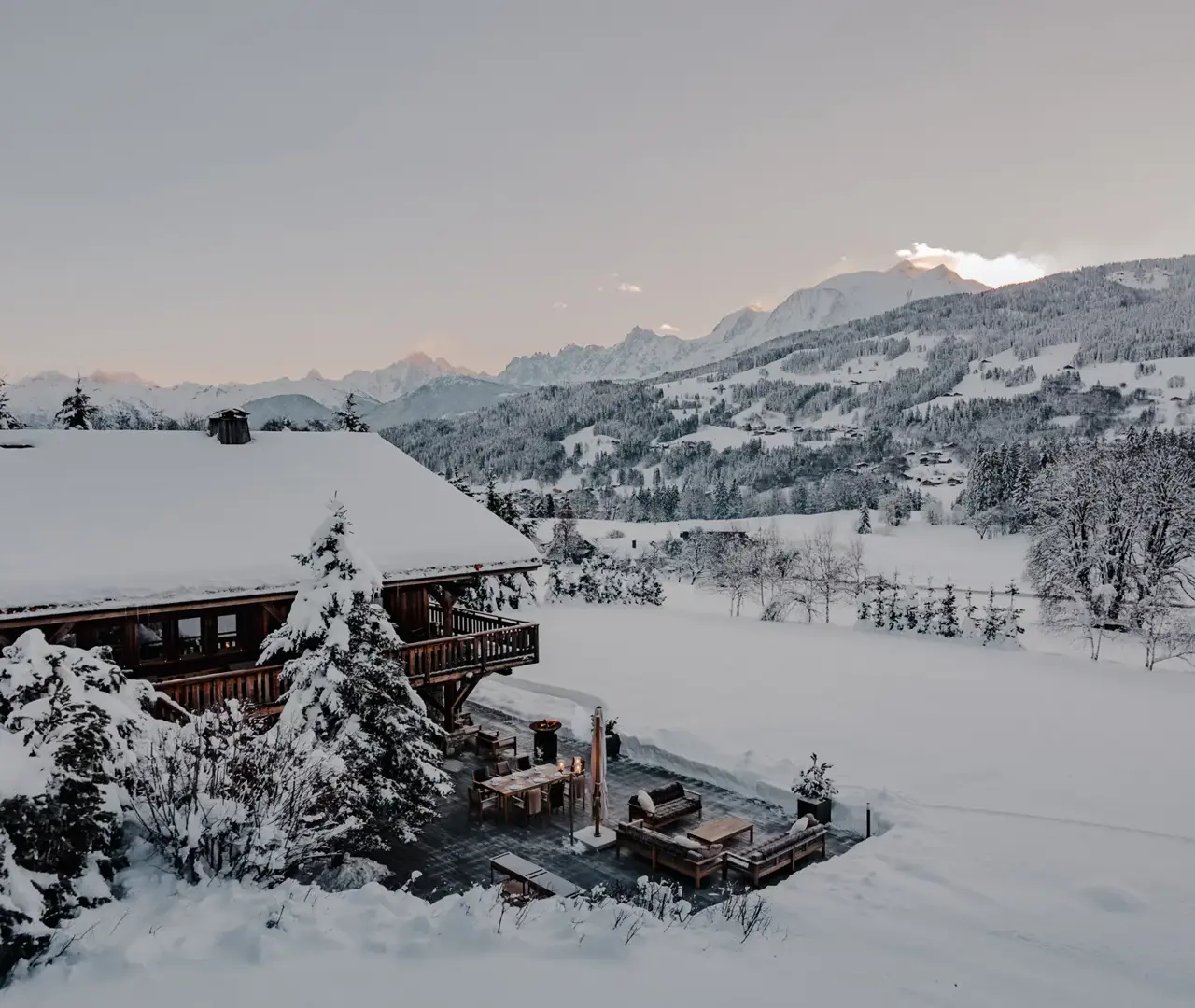 كوخ خشبي محاط بمنظر طبيعي مغطى بالثلوج عند غروب الشمس مع إطلالة بانورامية على جبال الألب الفرنسية.