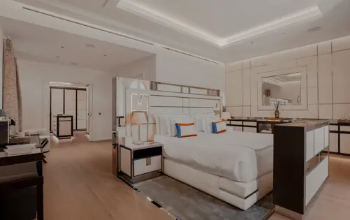 Chambre contemporaine élégante aux tons neutres avec tête de lit miroir, éclairage design et linge de lit luxueux rehaussé de coussins colorés.