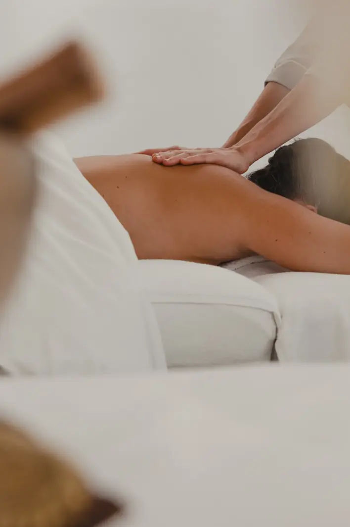 A relaxing spa scene showing a person receiving a back massage on a white treatment bed in a serene, softly lit environment.